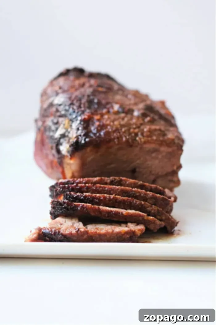 Ultimate Air Fryer Roast Beef 2 A perfectly roasted beef brisket with a dark, crispy, seasoned crust, partially sliced to reveal its juicy, tender interior. This delectable air fryer roast beef is presented on a white cutting board, ready to be served.
