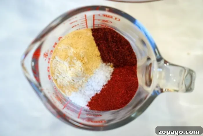 Ultimate Air Fryer Roast Beef 4 A top-down view of a glass measuring cup filled with four distinct spice portions: light beige, coarse white, and two shades of red. These fresh, colorful spices are perfectly arranged for creating a delicious dry rub for air fryer roast beef.