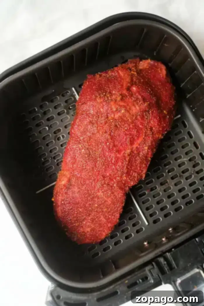 Ultimate Air Fryer Roast Beef 5 A seasoned beef roast, coated in a reddish-brown spice rub, resting perfectly inside a black air fryer basket with its signature perforated base for optimal air circulation during cooking.