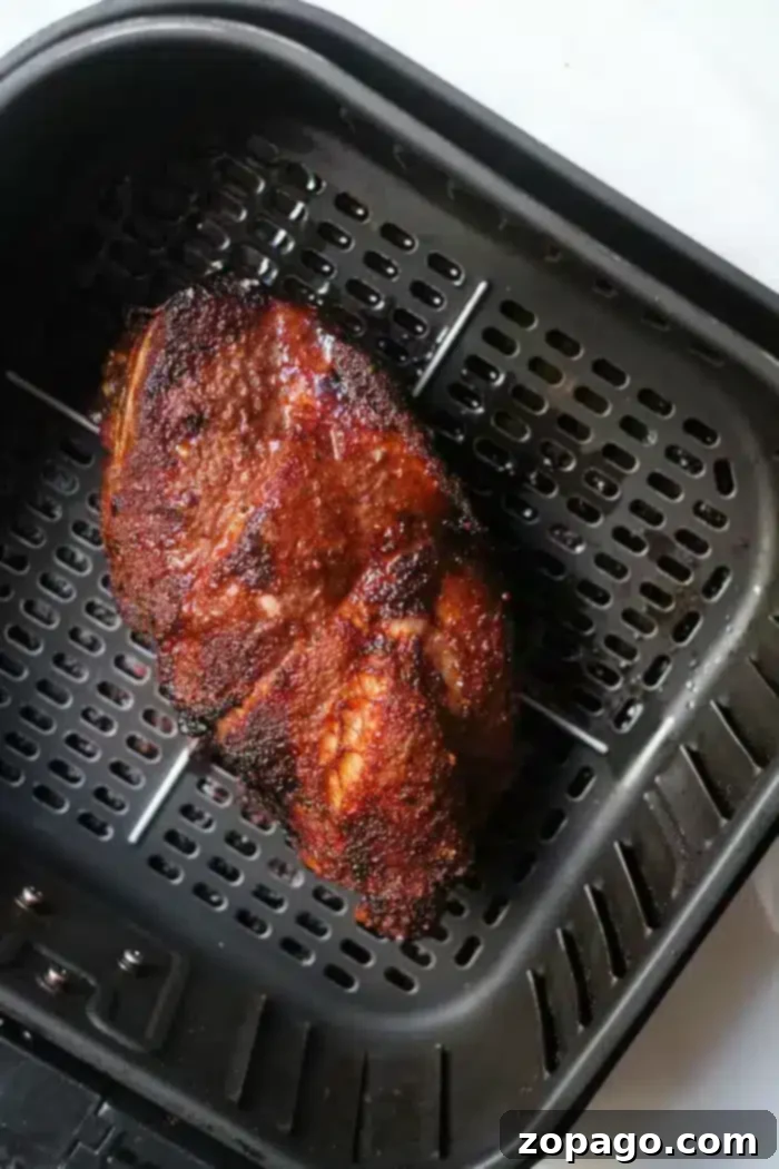 Ultimate Air Fryer Roast Beef 7 A succulent piece of cooked roast beef with a charred, crispy exterior, perfectly positioned inside a black air fryer basket after cooking.