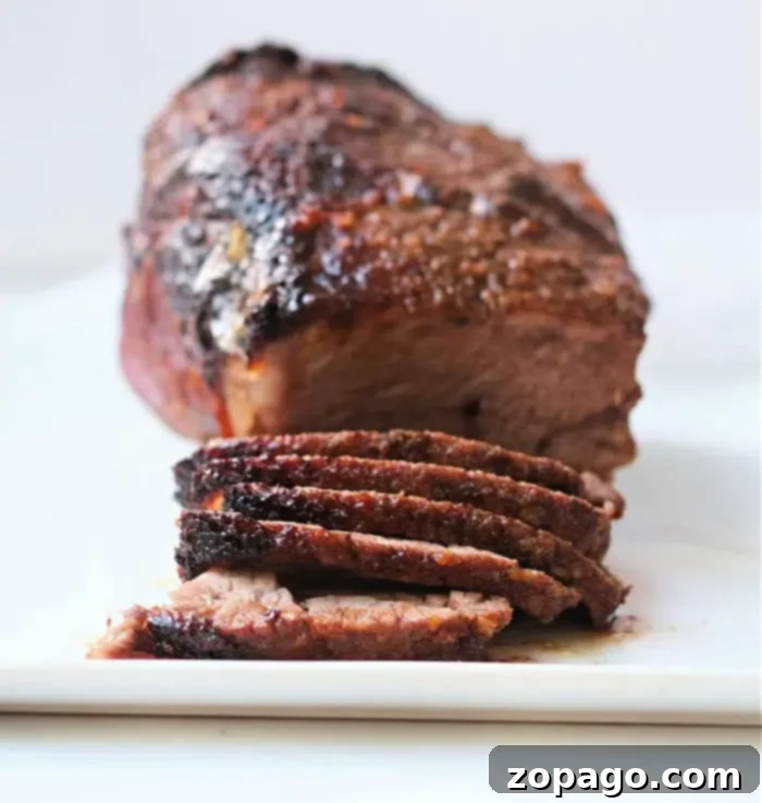 Ultimate Air Fryer Roast Beef 8 A beautifully roasted air fryer beef roast, perfectly browned on the outside, resting on a white surface with several appetizing slices already cut and displayed in the foreground.