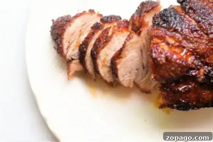 Crispy Air Fryer Pork Roast 7 Sliced, grilled meat with a charred brown exterior served on a white plate. The interior of the air fryer pork roast appears tender and juicy.
