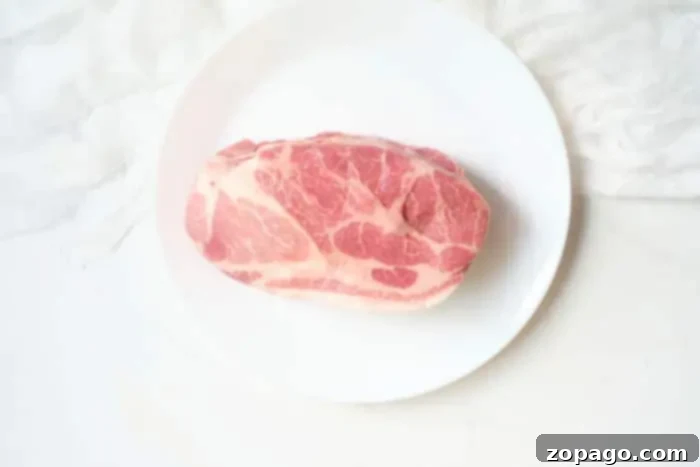 A raw cut of marbled pork roast, perfectly prepared for air frying, rests on a white plate with a textured fabric background, promising a succulent meal.