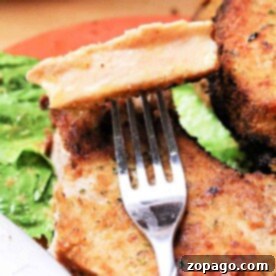 Crispy Air Fryer Pork Chops 8 Close-up of a fork holding a slice of breaded pork chop, perfectly crisped in the air fryer, with leafy greens on a plate.