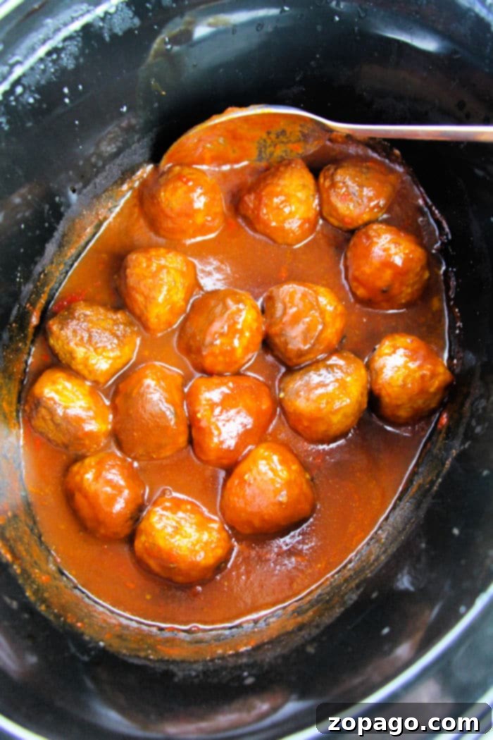 Grape Chili Glazed Meatballs 4 Savor the delectable crockpot grape jelly meatballs, simmering in a rich, reddish-brown sauce, perfectly presented with a spoon.