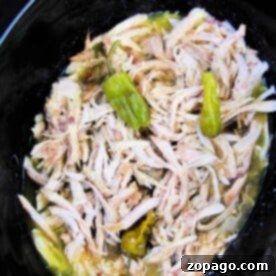 Pepperoncini chicken with shredded peppers simmering gently in a black slow cooker.
