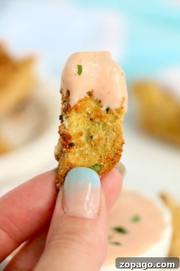 Close-up of a hand holding a perfectly breaded and golden-brown air fryer artichoke heart, ready to be eaten.