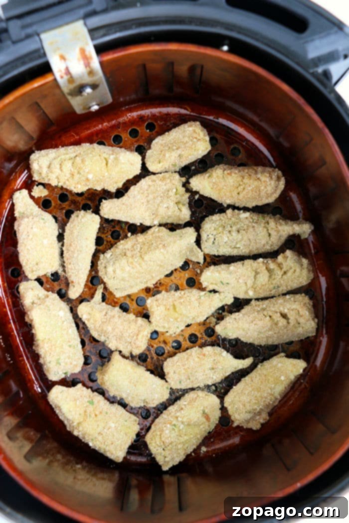 Crispy, golden-brown breaded artichoke hearts arranged in an air fryer basket, alongside some unbreaded hearts.