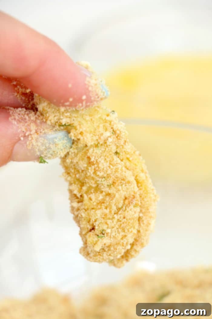 Crispy Air Fried Artichoke Hearts 8 A hand holds a breaded artichoke heart piece above a bowl of breadcrumbs, illustrating the breading process for air fryer artichoke hearts.