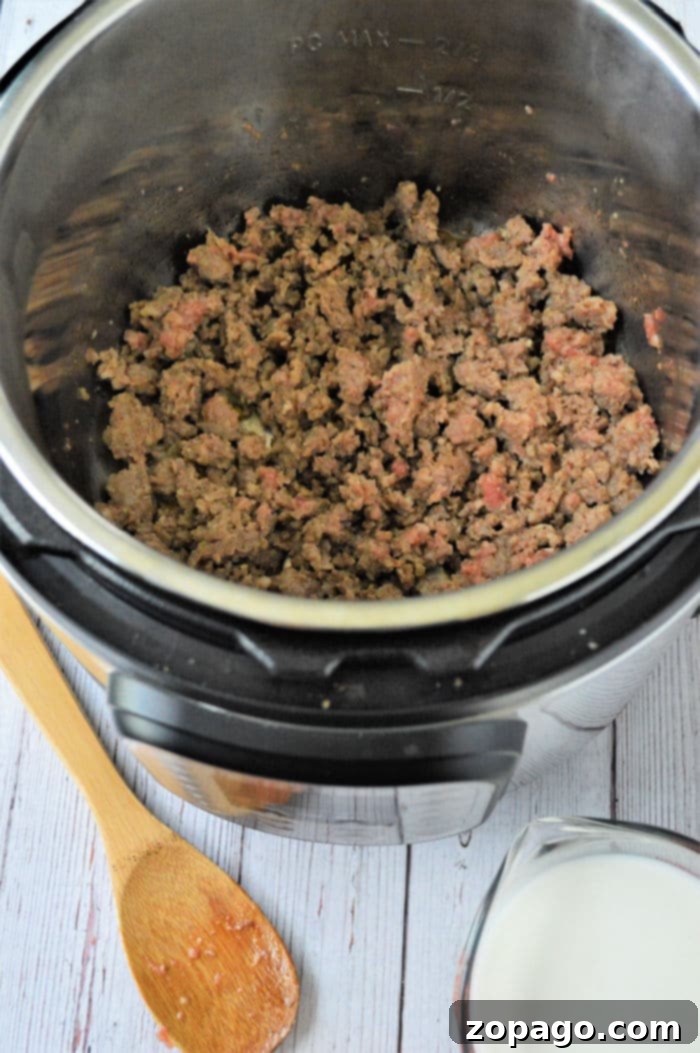 Effortless Instant Pot Sausage Gravy 5 Close-up view of ground sausage browning in an Instant Pot, with some liquid added for deglazing the pot, showing the process of building flavor for Instant Pot sausage gravy.
