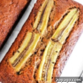 A loaf of ginger banana bread with sliced bananas on top rests elegantly on a pristine white surface.