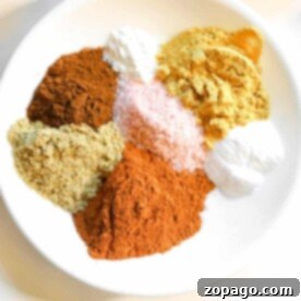 A white plate with piles of vibrant spice powders, including homemade gingerbread spice ingredients, and coarse salt, arranged artfully.