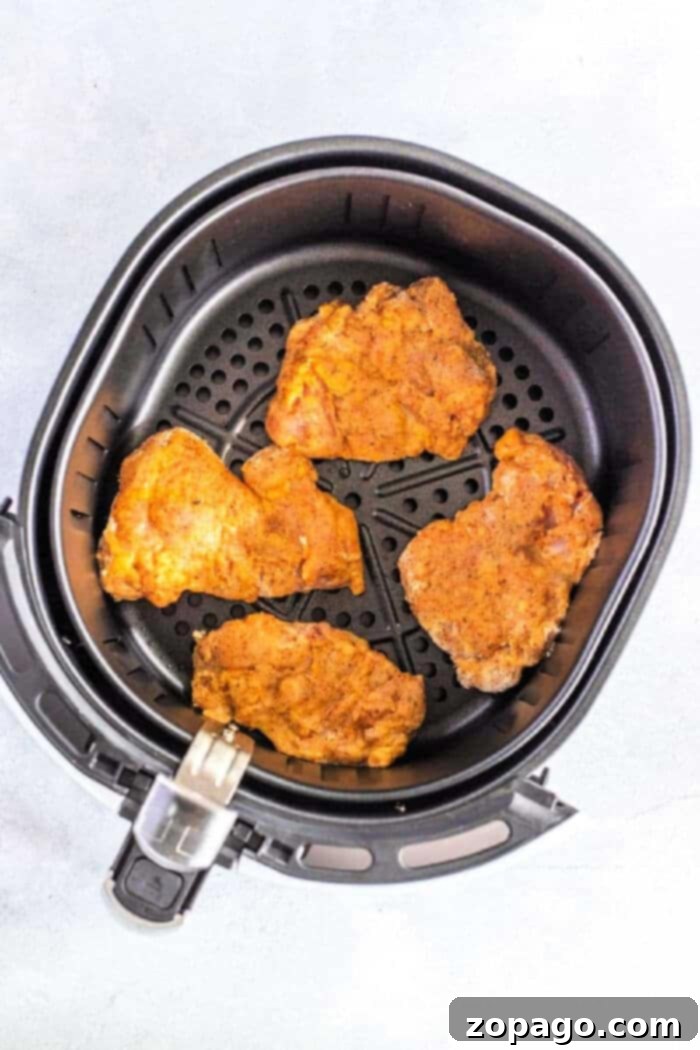 Crispy Air Fryer Chicken Thighs 2 Four seasoned chicken thighs sit invitingly in an air fryer basket, their crispy edges reminiscent of perfectly cooked fried chicken thighs.