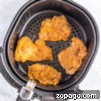 Four perfectly seasoned chicken thighs nestled in an air fryer basket, ready to transform into crispy fried delights.