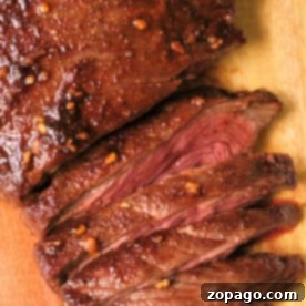Savory Dry Rub Air Fryer Flank Steak 8 Sliced, juicy flank steak with a seared crust and garlic seasoning sits elegantly on a wooden cutting board, reminiscent of perfectly cooked air fryer flank steak.