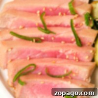 Slices of seared ahi tuna steak with sesame seeds and green garnishes on a white plate, prepared perfectly in an air fryer.