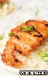 A plate with white rice topped with sliced, air fryer chicken katsu drizzled with dark sauce and garnished with sliced green onions.