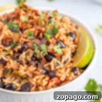 A bowl of rice mixed with instant pot black beans, diced vegetables, and garnished with cilantro and lime wedges.