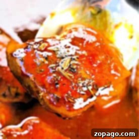 Effortless Slow Cooker Boneless Skinless Chicken Thighs 7 A close-up of a spoon lifting a glazed boneless skinless chicken thigh from the crockpot, covered in sauce and herbs.