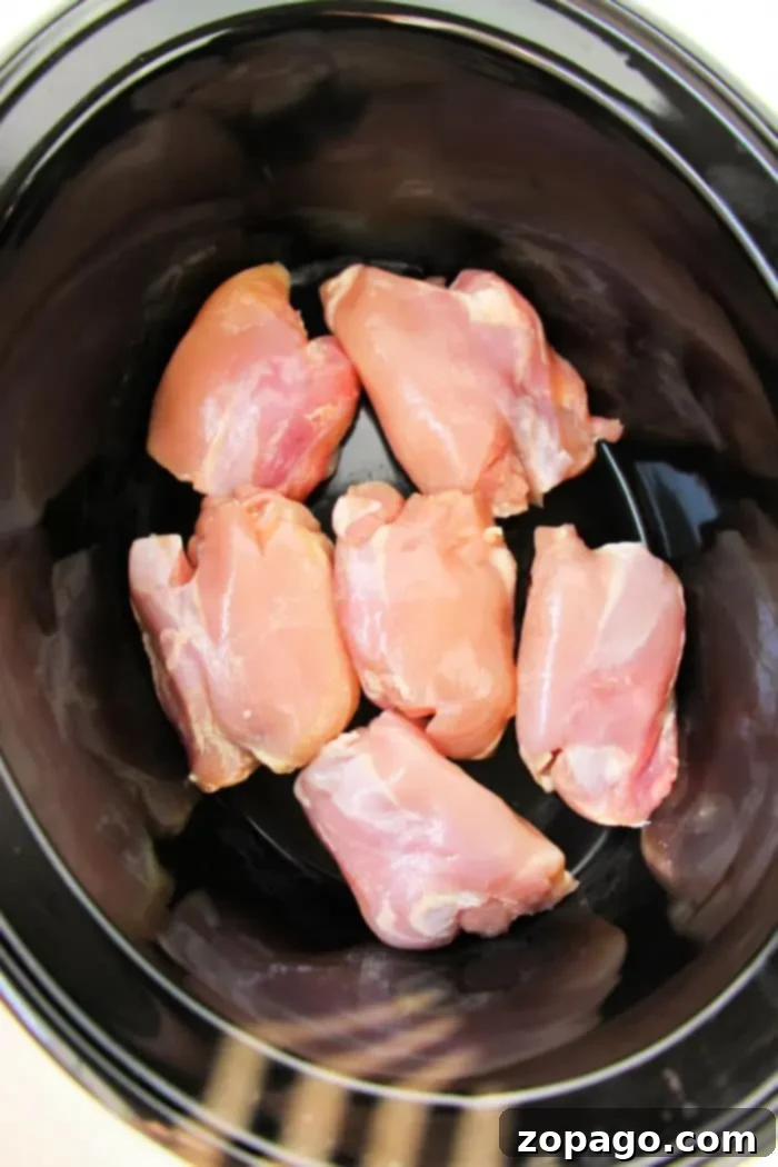 Effortless Slow Cooker Boneless Skinless Chicken Thighs 9 Boneless, skinless chicken thighs nestled in a black crockpot await their transformation into a delicious meal.