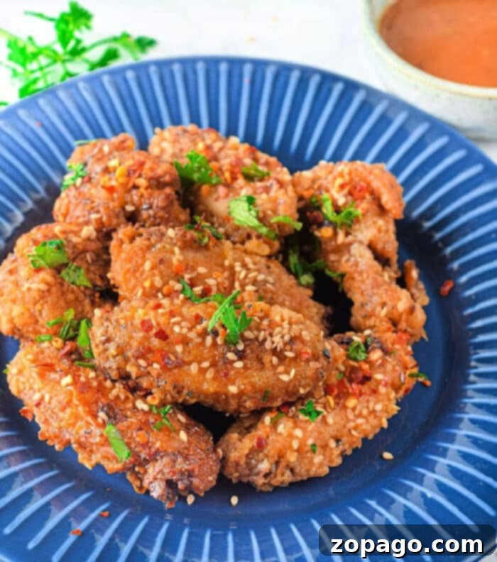 Dynamite Chicken 2 Crispy firecracker air fryer chicken wings garnished with sesame seeds and fresh parsley on a vibrant blue plate, ready to be served.