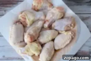 Dynamite Chicken 6 A collection of raw chicken wings and drumsticks are laid out on a white paper towel on a rustic, white wooden table.