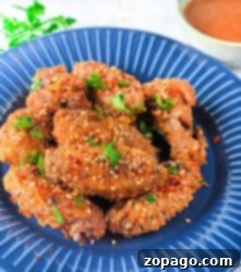 Dynamite Chicken 9 Crispy firecracker air fryer chicken wings garnished with sesame seeds and parsley on a blue plate.
