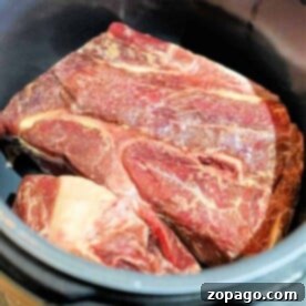 A frozen chuck roast, beautifully marbled, sits in the pressure cooker pot, ready for magic in the Instant Pot.
