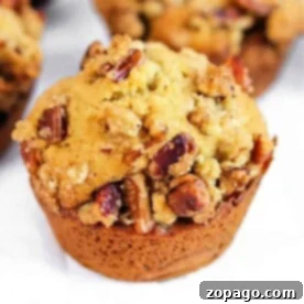 Spiced Sweet Potato Muffins 6 A close-up of a sweet potato muffin with a crumbly top and pecans, set on a light surface.