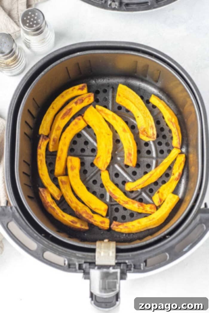 Crispy Air Fryer Pumpkin Fries 6 Curved slices of air fryer pumpkin in a basket, with salt and pepper shakers nearby, ready for seasoning.
