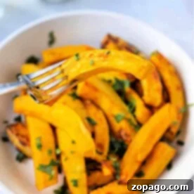A bowl of roasted pumpkin wedges, perfectly crisped in the air fryer, is garnished with herbs. A fork holds one golden wedge above the bowl.