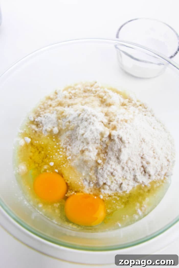 Zesty Lemon Crinkle Cookies 3 Assorted ingredients for lemon crinkle cookies, including butter, cream cheese, sugar, eggs, and a fresh lemon, laid out on a wooden surface.