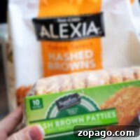 Close-up of a hand holding a box of frozen hash brown patties in front of an Alexia package, perfect for crispy perfection in the air fryer.
