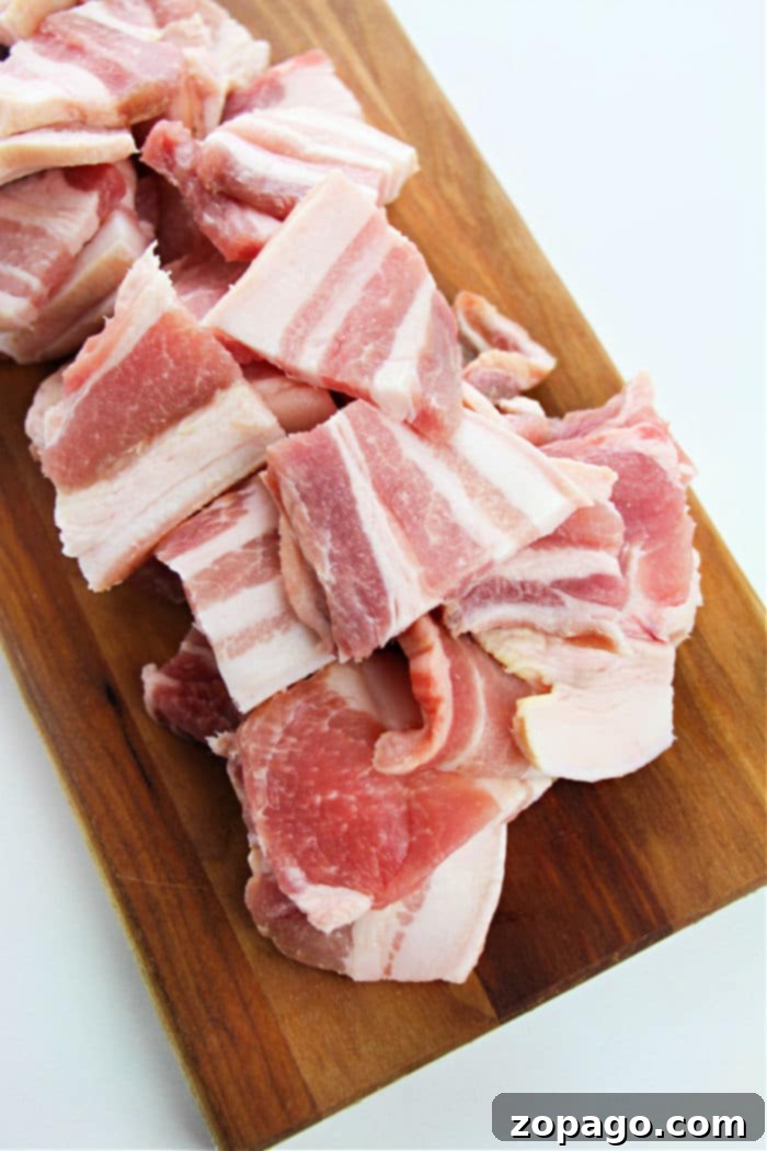 Succulent and Crispy Oven Pork Belly 4 Chopped raw pork belly slices rests on a wooden cutting board, inviting thoughts of how to cook pork belly in the oven for a savory treat.