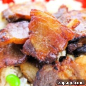 A close-up of crispy pork belly, oven-cooked to perfection, on rice with green peas, served on a vibrant red plate.