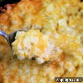 A spoon scoops up a cheesy potato casserole, rich with creamy hashbrown potatoes, all topped with perfectly melted cheese.