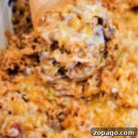 A spoon serving a cheesy baked hamburger and rice casserole with ground meat and pasta from a dish.