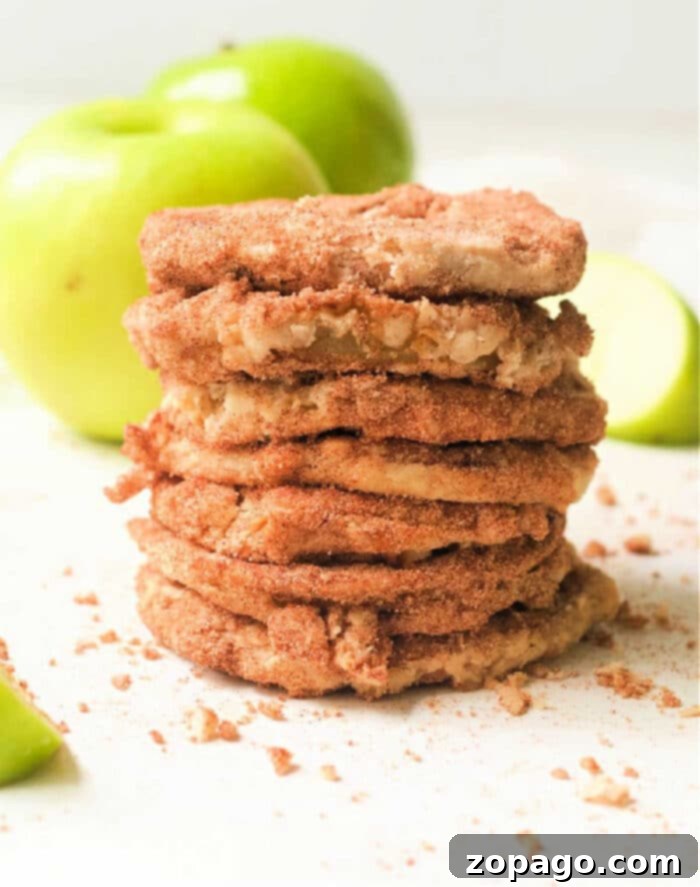 Perfect Air Fryer Apples 2 A stack of golden brown, crispy air fryer apple slices, dusted with cinnamon sugar, sits invitingly on a plate with fresh green apples in the background, highlighting the delightful crunch and sweetness that air frying brings to this healthy snack or dessert.