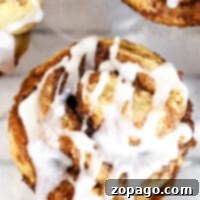 Close-up of a cinnamon roll muffin topped with white icing, revealing its swirled layers.