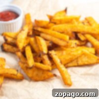Crispy Roasted Turnip Sticks 4 Golden baked turnip fries on parchment paper, crisped to perfection in the air fryer, with a small cup of ketchup in the background.