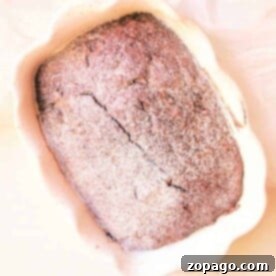 A freshly baked loaf of chocolate gingerbread cake in a scalloped baking dish, dusted with flour.