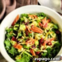 A white bowl of leafy salad with Brussels sprouts, pecans, cranberries, and bacon bits sits on a tablecloth with a spoon nearby.