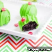 How the Grinch Stole Dessert 7 Green cake balls on a plate, one bitten, with heart sprinkles evoke a whimsical grinch dessert vibe against a zigzag pattern tablecloth.