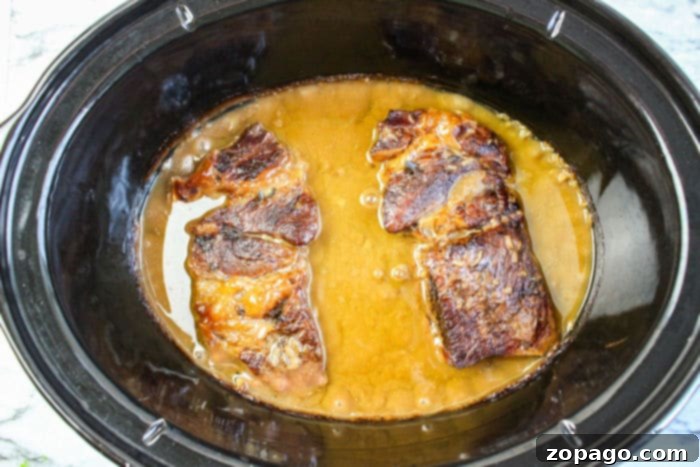 Fall-Apart Tender Slow Cooker Roast Beef and Savory Gravy 7 Two browned chuck roast and gravy simmers in a black slow cooker, melding rich flavors with a savory gravy.