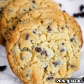 Four Bisquick chocolate chip cookies rest on a white surface, surrounded by scattered chocolate chips.
