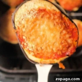 A close-up of a slice of air fryer eggplant parm, topped with rich tomato sauce and melted cheese, resting perfectly on a spoon.