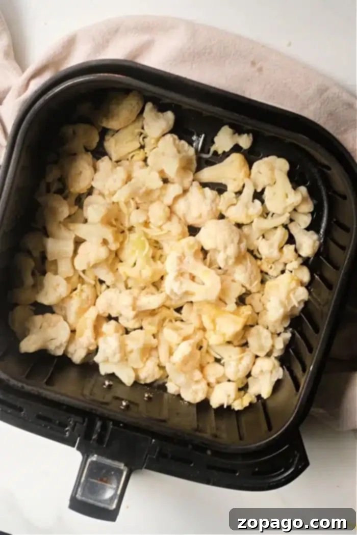 Perfectly Tender Air Fryer Frozen Cauliflower 6 Crispy frozen cauliflower florets cooking in an air fryer basket
