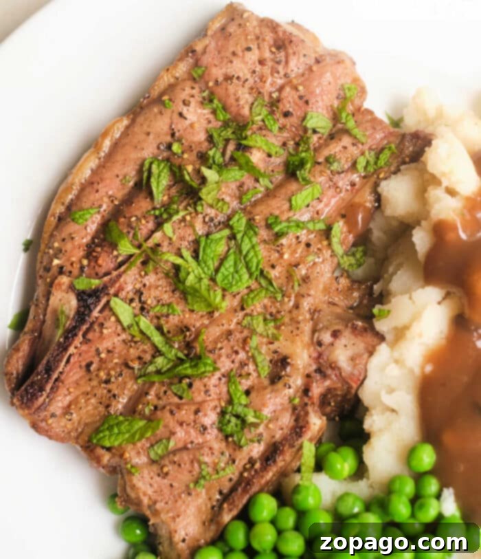Ninja Foodi lamb chops in the air fryer, seasoned with herbs, served alongside creamy mashed potatoes, rich gravy, and a side of peas on a white plate.