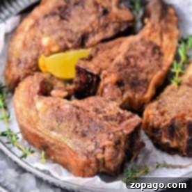 Four perfectly seasoned lamb chops, cooked to tender perfection in an air fryer, rest on a plate adorned with a lemon wedge and fresh thyme sprigs.