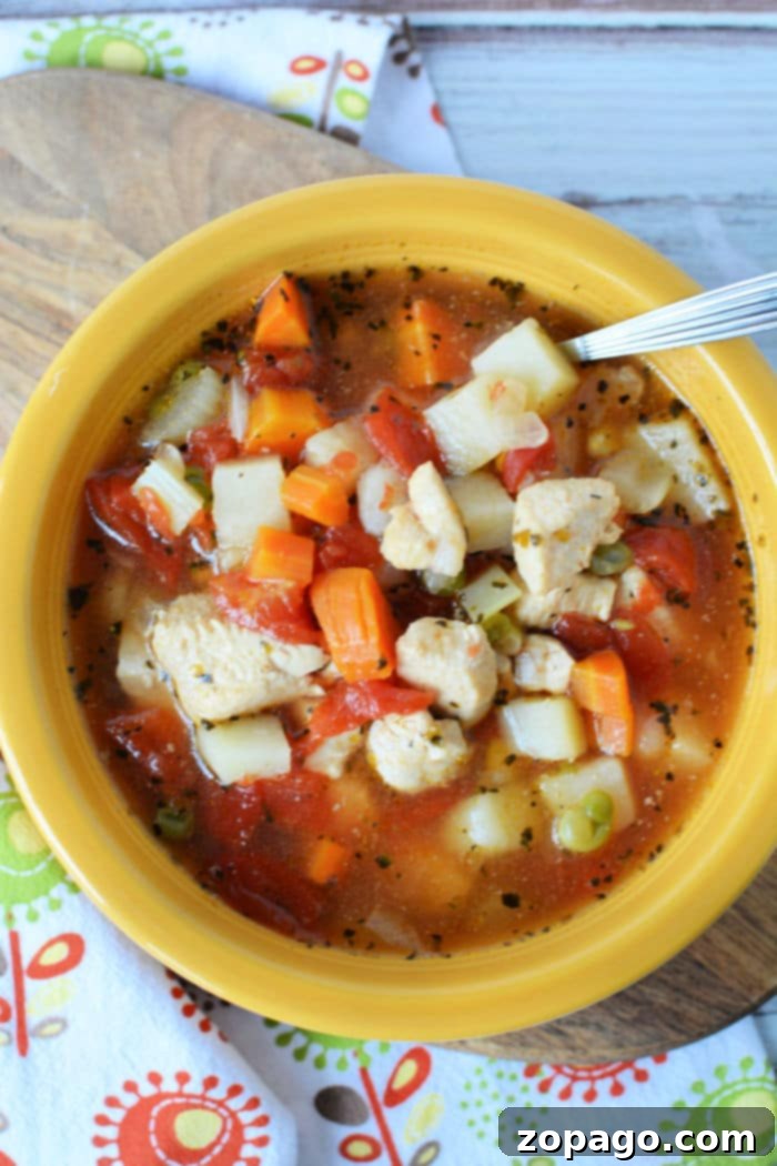 Hearty Instant Pot Chicken Vegetable Soup 2 A vibrant yellow bowl of Instant Pot chicken vegetable soup, richly filled with tender diced potatoes, carrots, tomatoes, and peas, with a spoon gently resting within. The bowl is beautifully presented on a decorative patterned cloth.